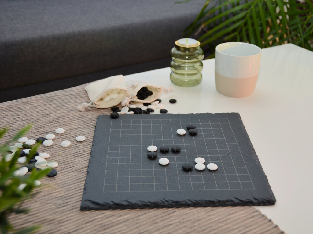 Baduk Spielsituation 13x13: Strategisch platzierte Steine auf dem gravierten Raster in seitlicher Ansicht.