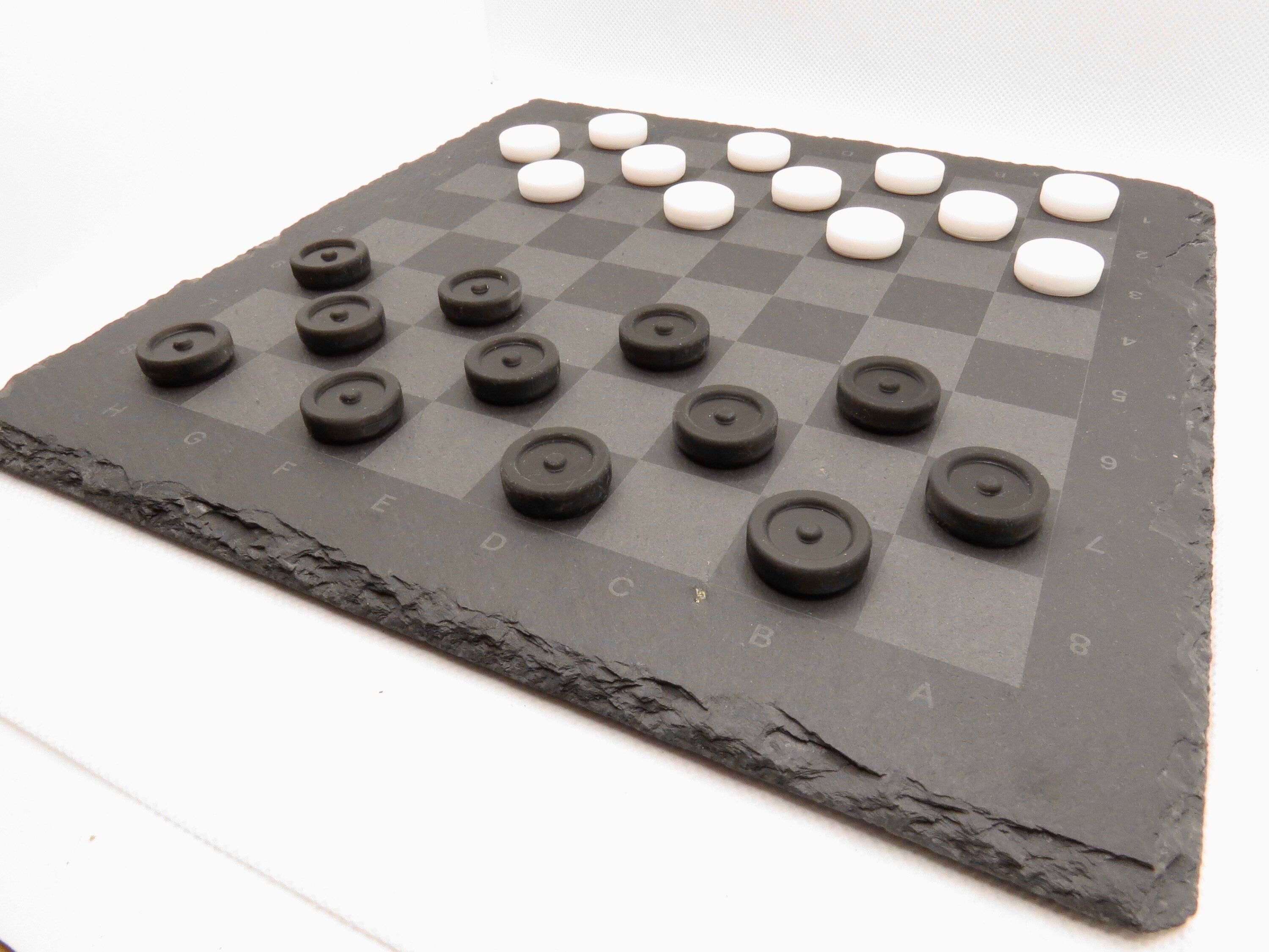 Aufgebautes Dame-Spiel seitlich: Modernes Design des Strategie-Klassikers auf grauer Steinplatte.