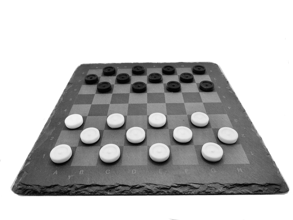 Dame Spiel aus Schiefer: Edles Brettspiel-Set mit weißen und schwarzen Spielsteinen auf dunklem Naturstein.