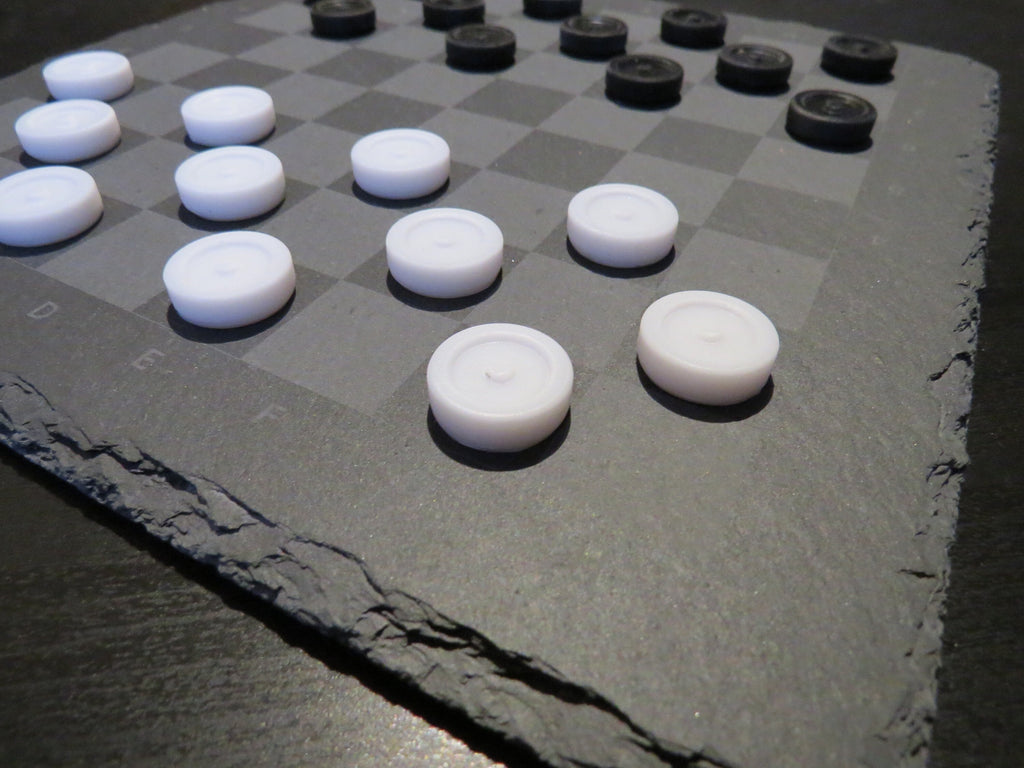 Nahaufnahme Dame Spielsteine: Strukturierte Schieferoberfläche mit lasergraviertem Raster und flachen Spielsteinen.