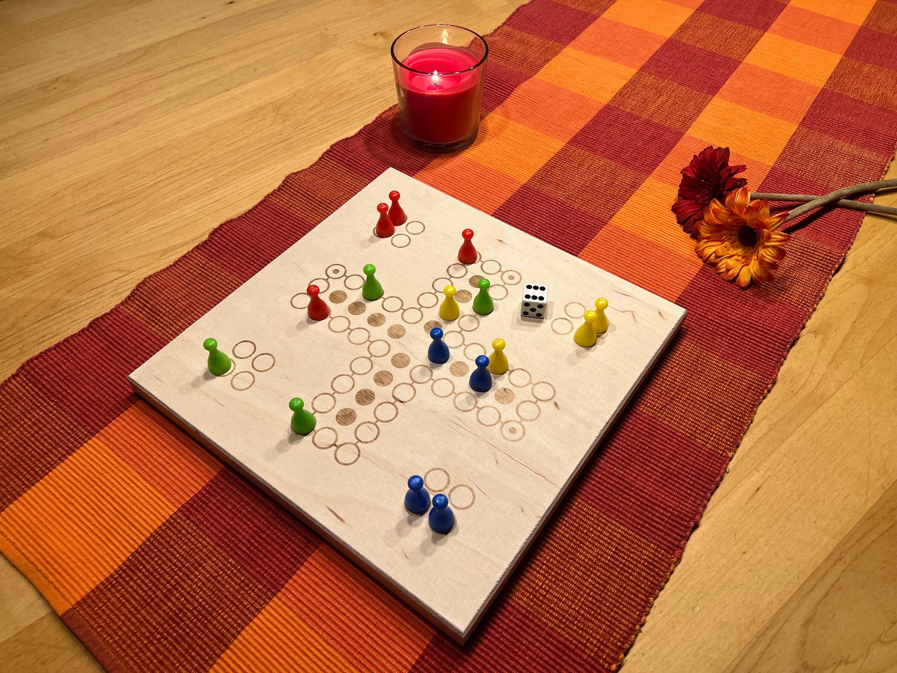 Gemütlicher Spieleabend: Ludo Holzbrettspiel auf dem Wohnzimmertisch bei Kerzenschein dekoriert.