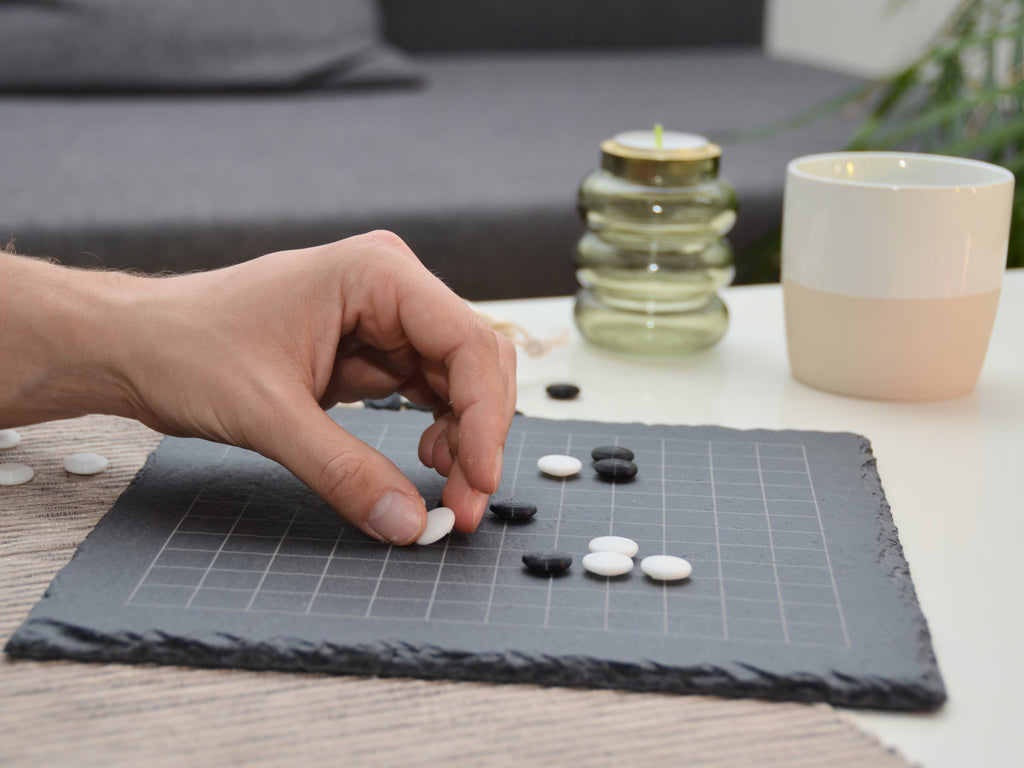 Person spielt Go (Weiqi) am Tisch: Hand setzt weißen Spielstein auf das 13x13 Schieferbrett.