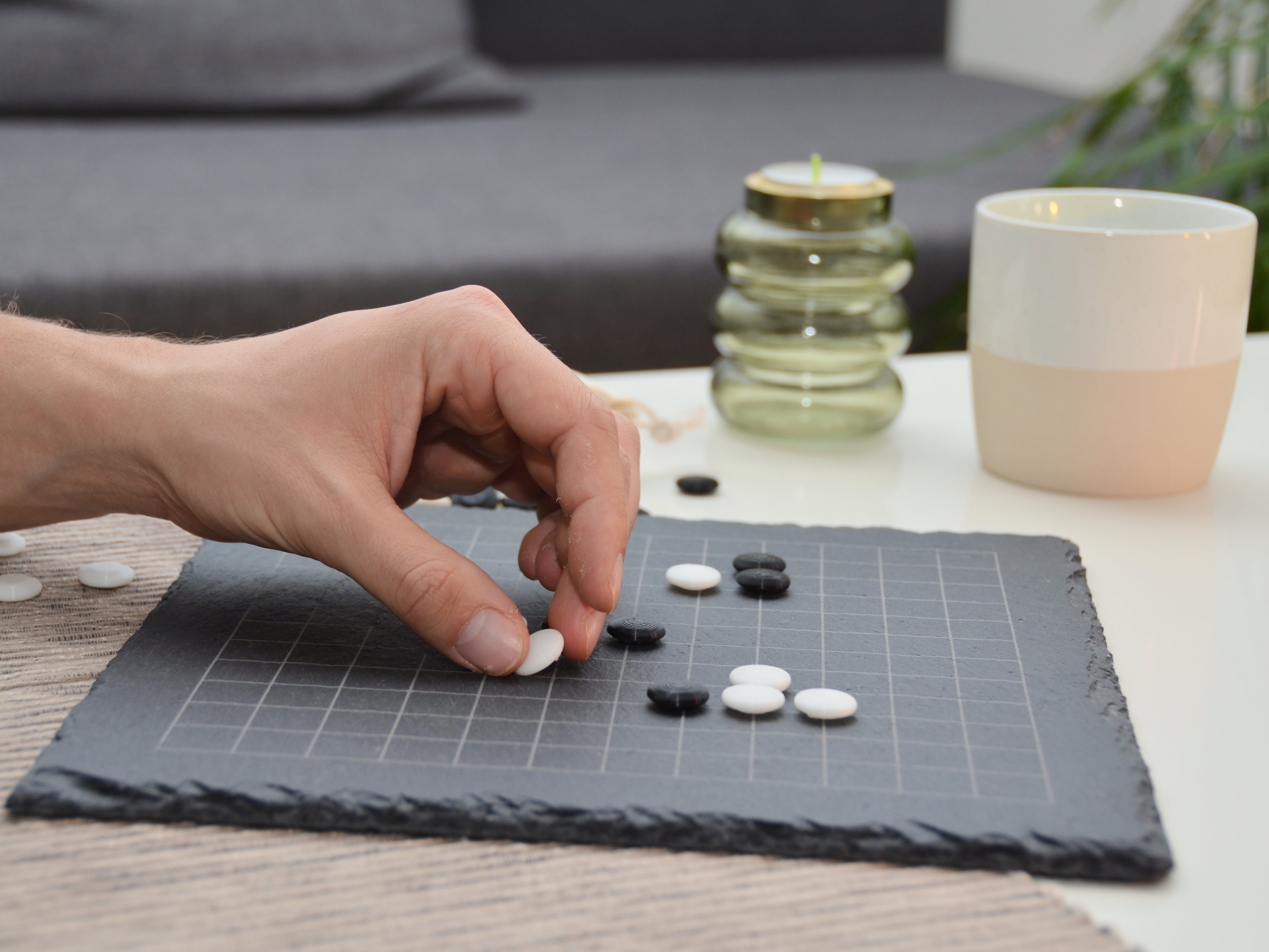 Person spielt Go (Weiqi) am Tisch: Hand setzt weißen Spielstein auf das 13x13 Schieferbrett.