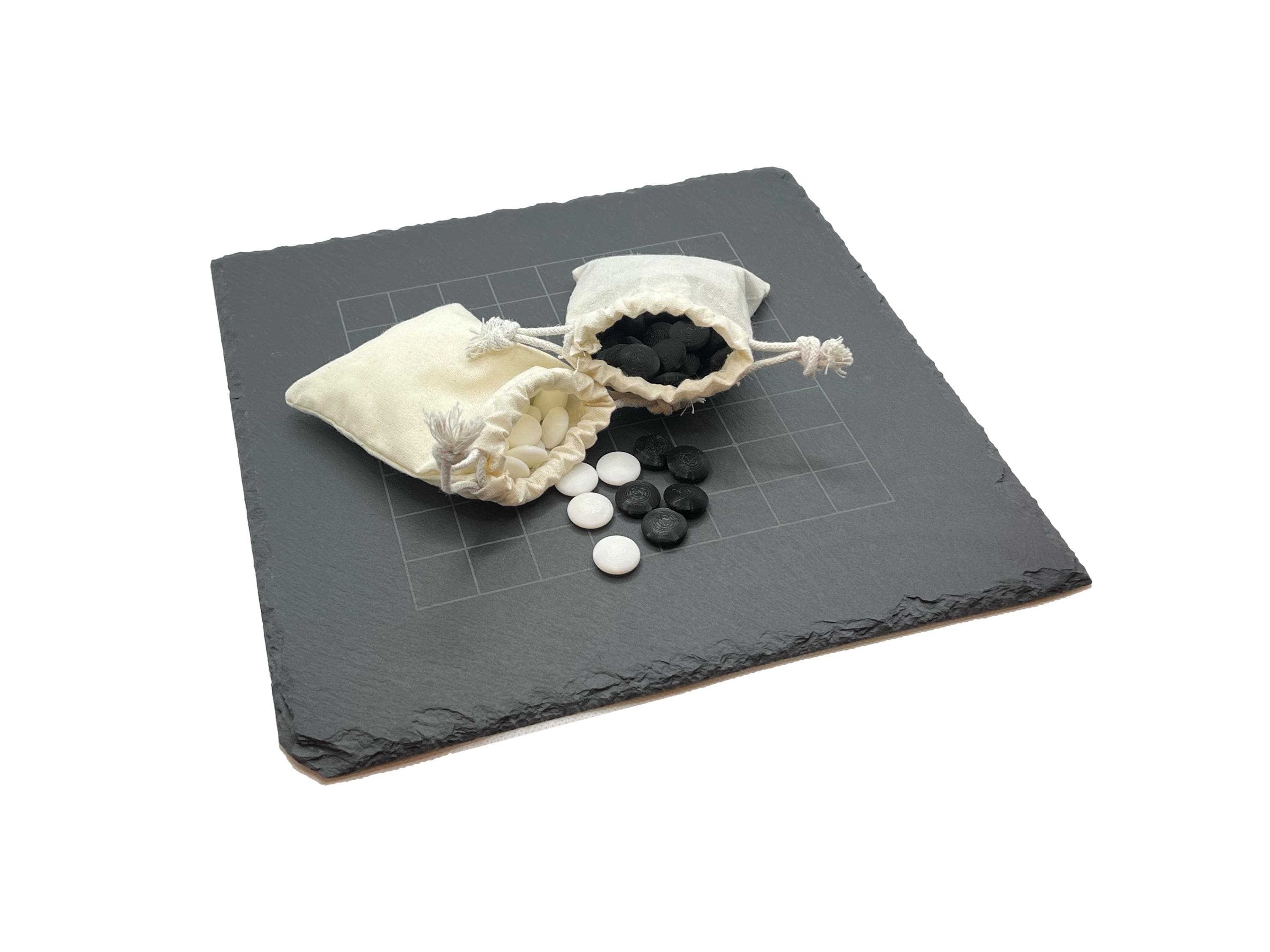 Zubehör für Go-Spiel: Zwei Jutesäckchen mit Spielsteinen auf dem dunklen Steinbrett liegend.