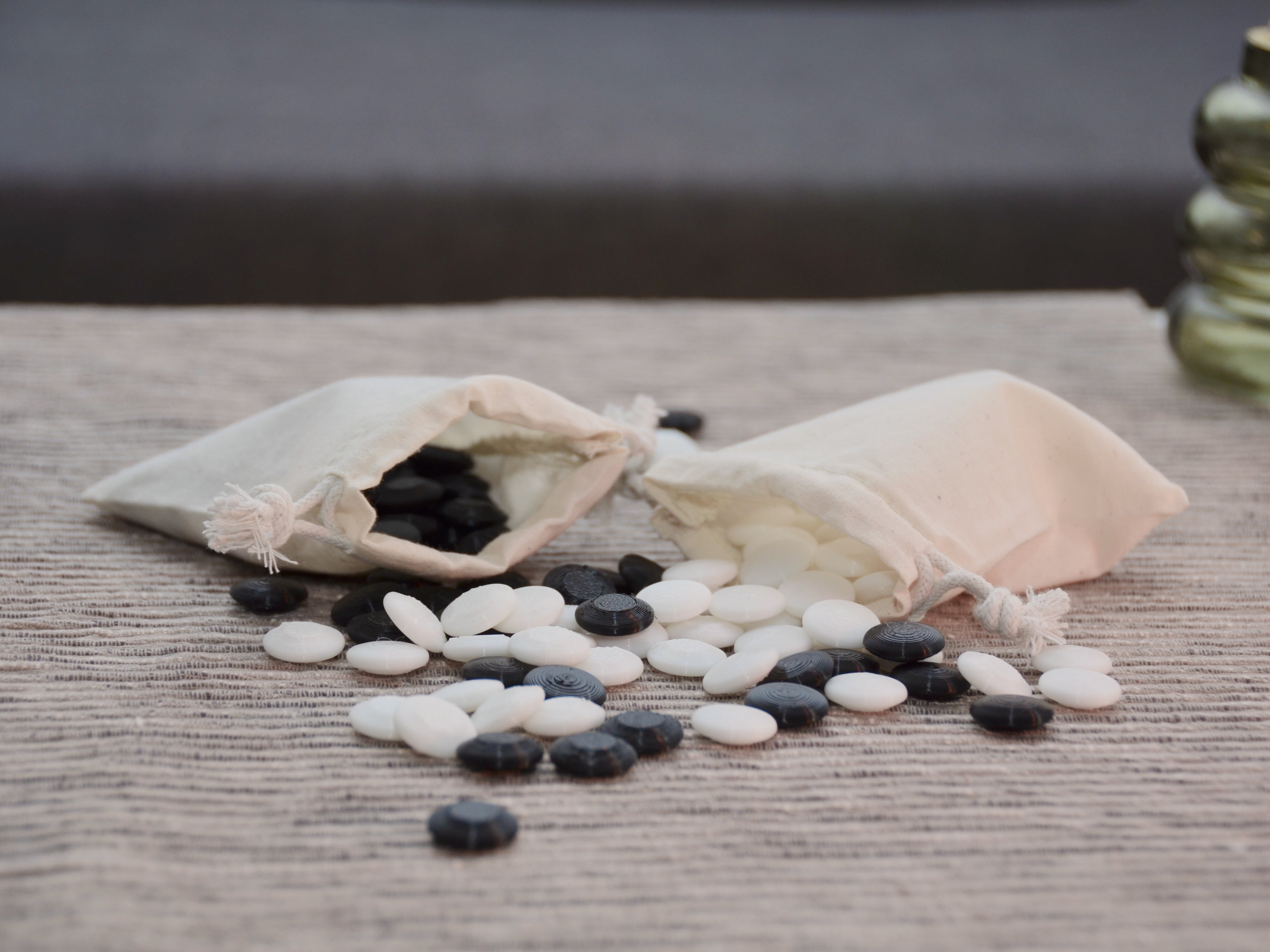 Go Spiel Zubehör: Jutesäckchen und schwarz-weiße Linsensteine auf der Maserung des Holzbretts.
