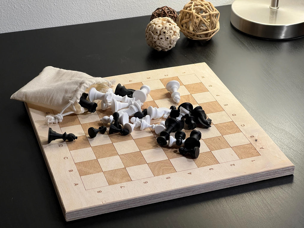 Holz Schachspiel Set: Helles Echtholz-Brett mit verstreuten schwarzen und weißen 3D-Druck Figuren und Stoffbeutel.