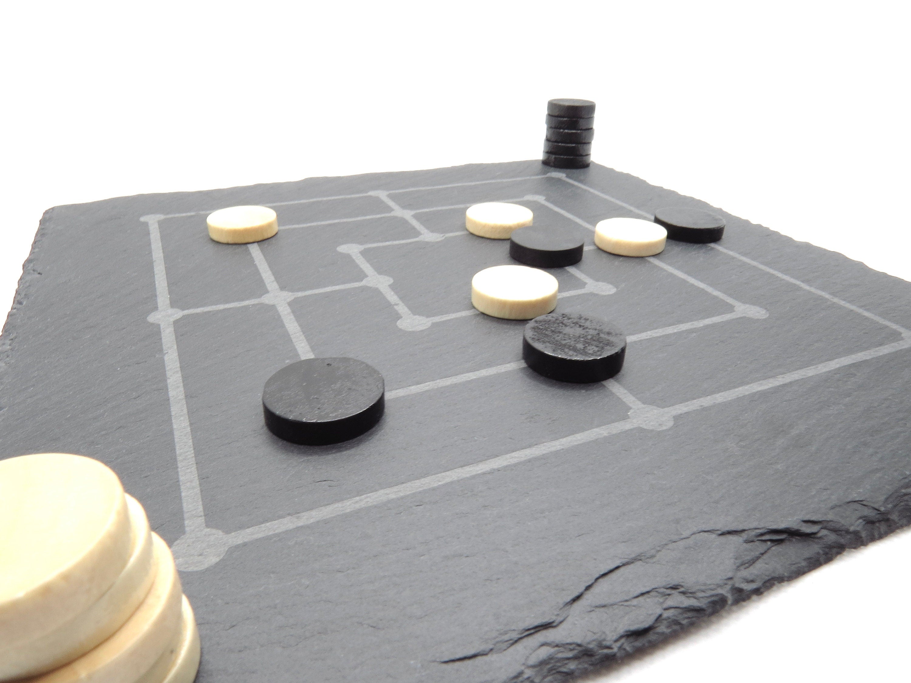 Aufgebautes Mühle-Brettspiel auf Schieferplatte: Strategie-Klassiker mit modernen Spielsteinen in Spielsituation.