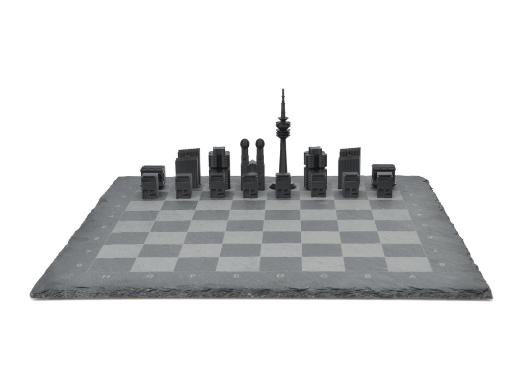 Frontalansicht München Schachspiel komplett aufgebaut: Schwarze und weiße Skyline-Figuren gegenübergestellt auf Schieferplatte.